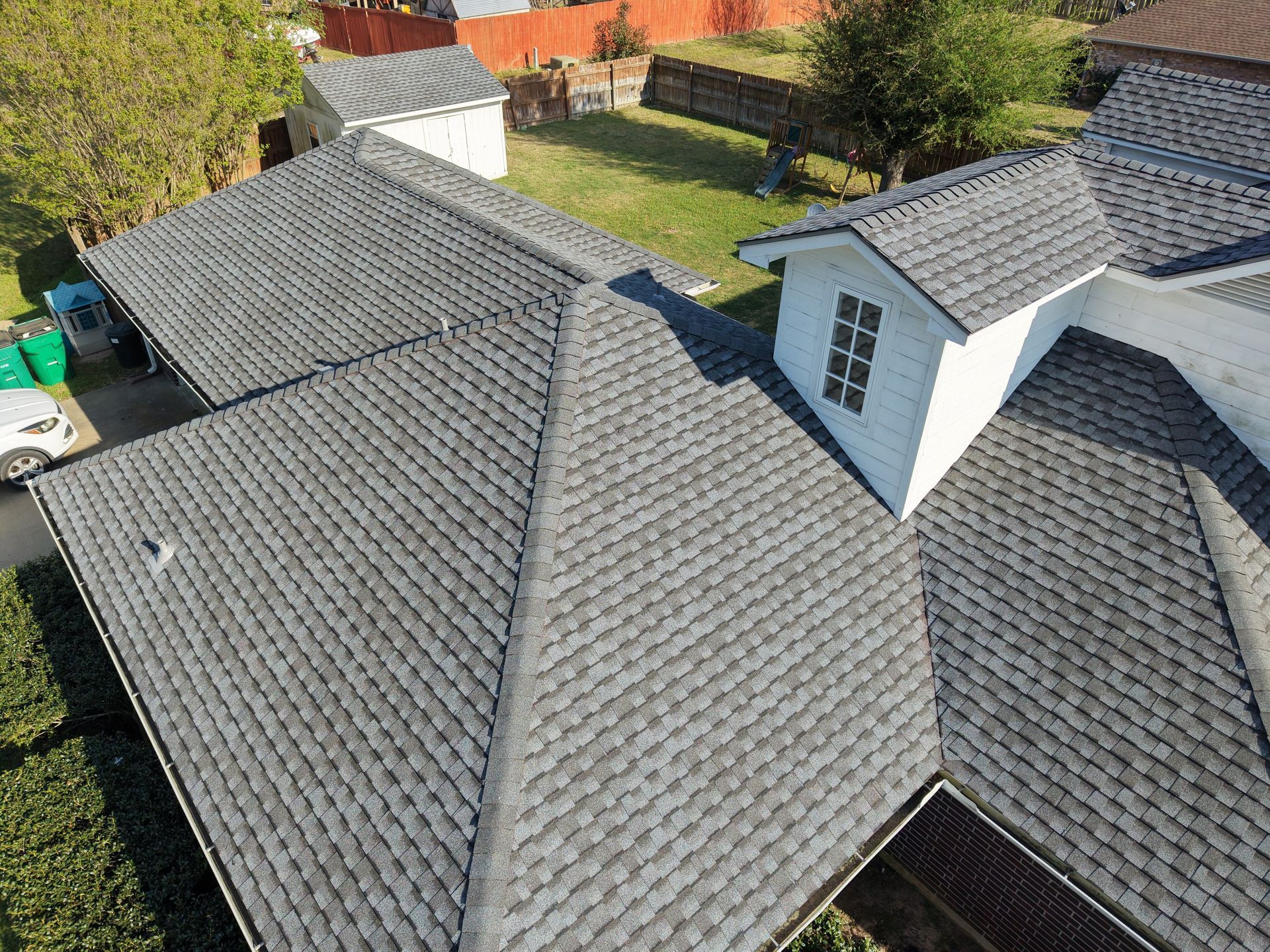 Aerial view of a gray shingled house roof with two dormer windows and a red fence in the background
