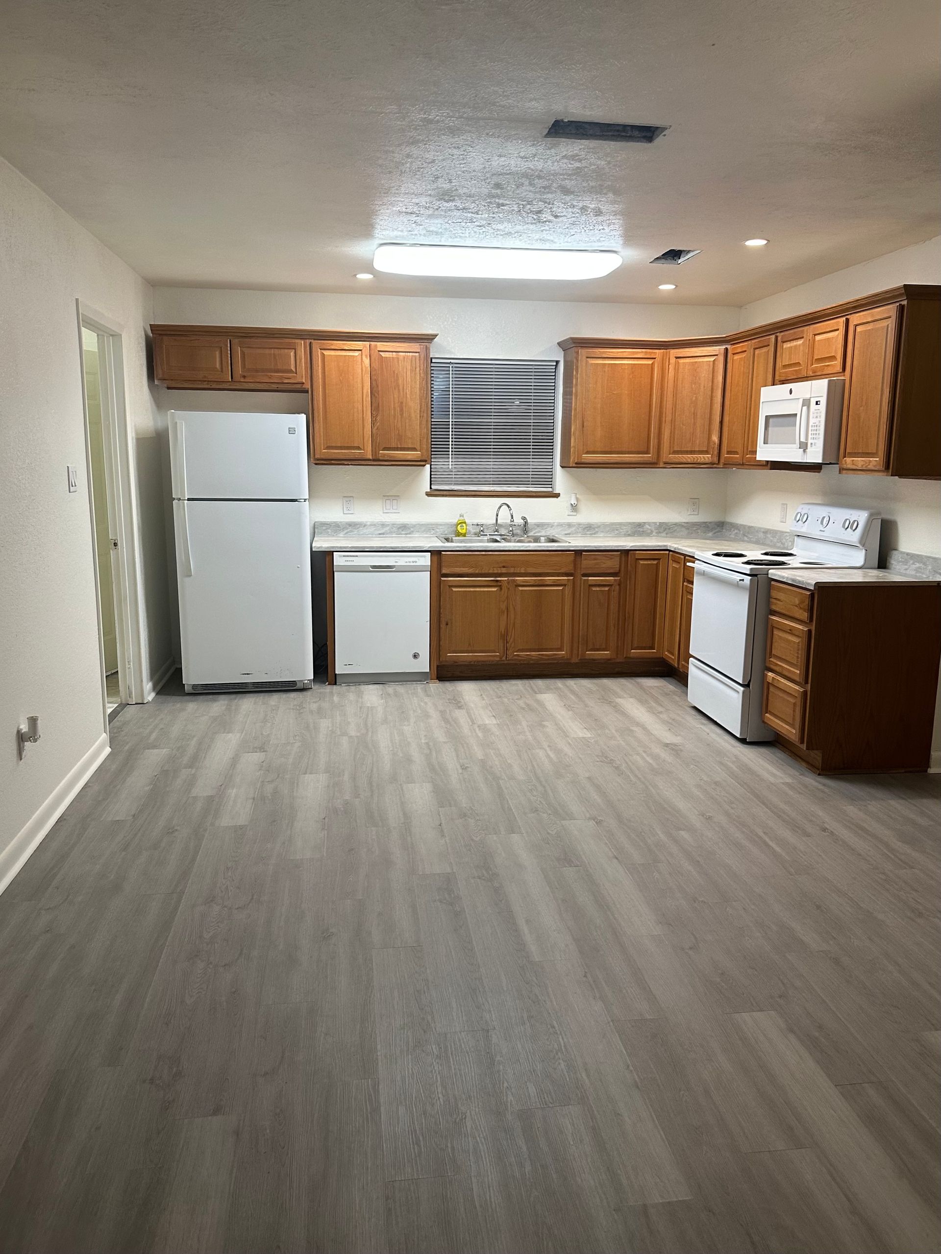 Empty kitchen with wood cabinets, white appliances, and gray flooring in a small apartment