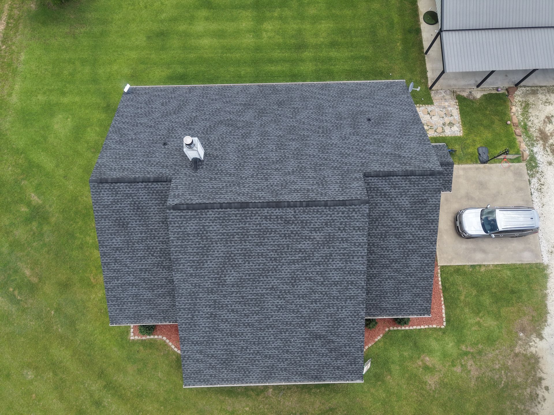 Aerial view of a house with a dark gray roof, green lawn, and a white car parked beside the driveway.