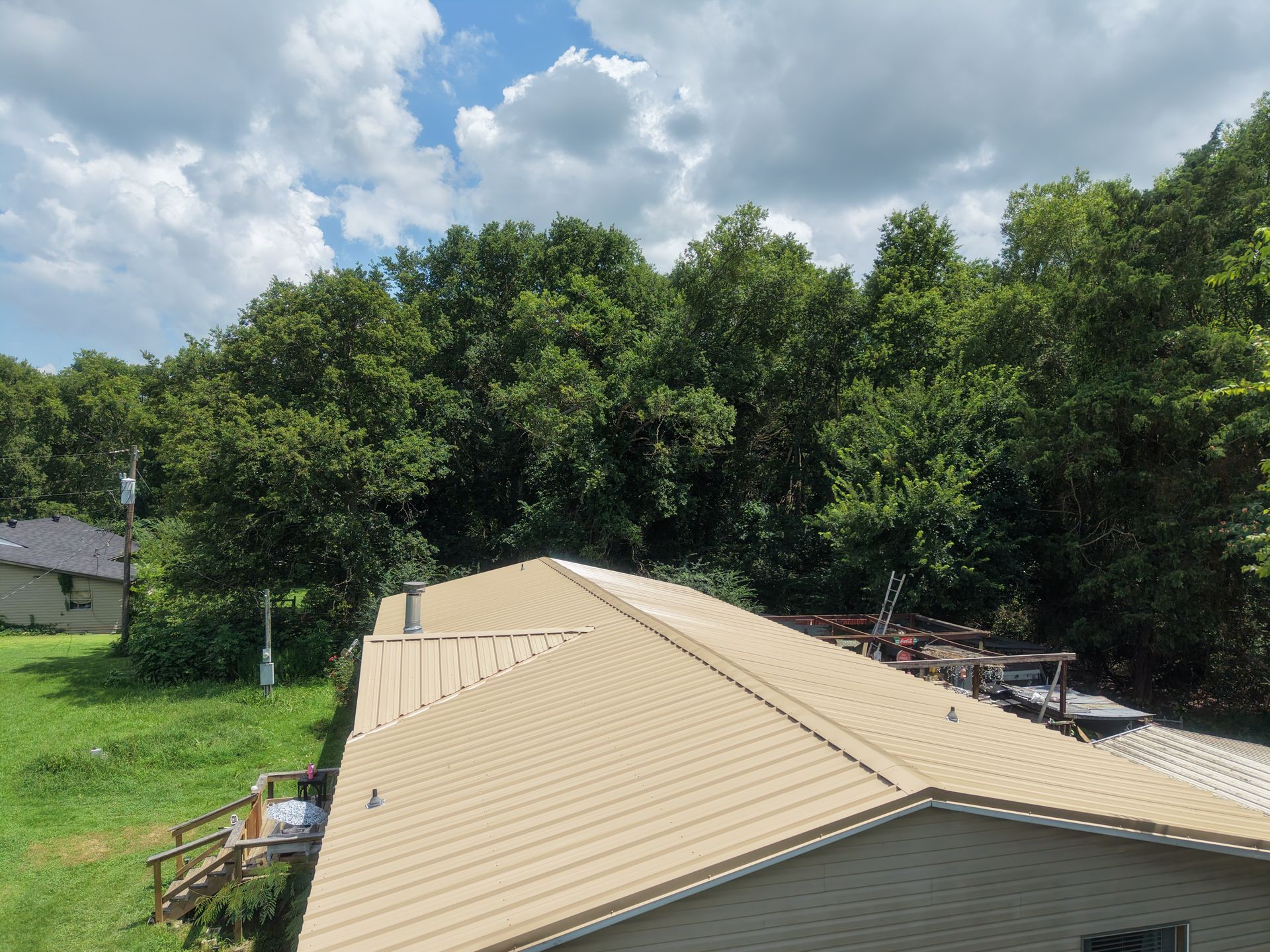 Beige metal roof in a wooded neighborhood under a cloudy sky