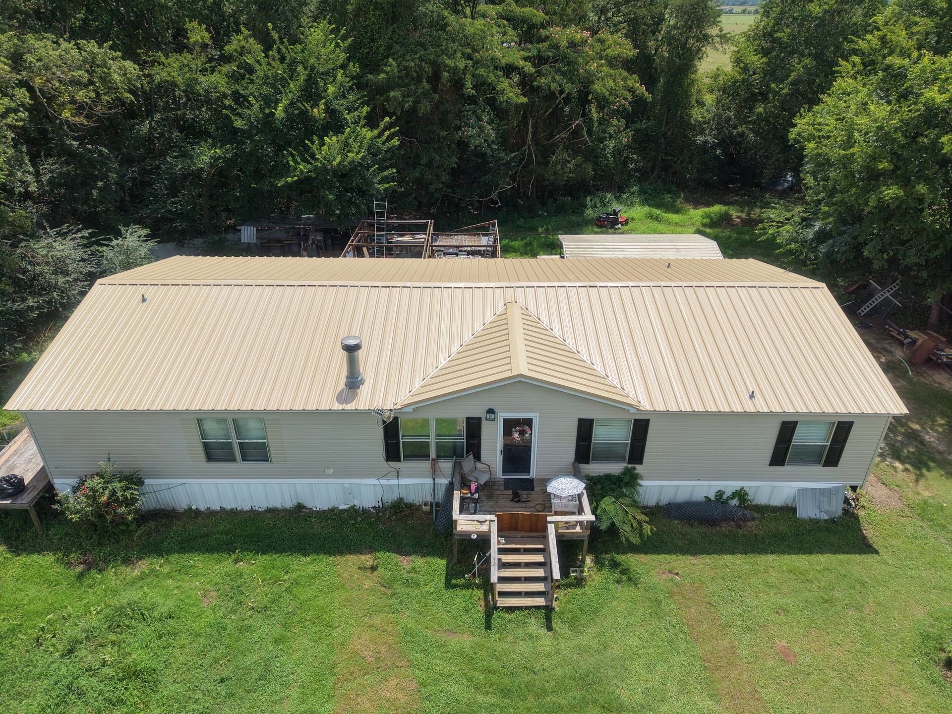 Aerial view of a white house with a tan roof, front porch, and green lawn surrounded by trees.