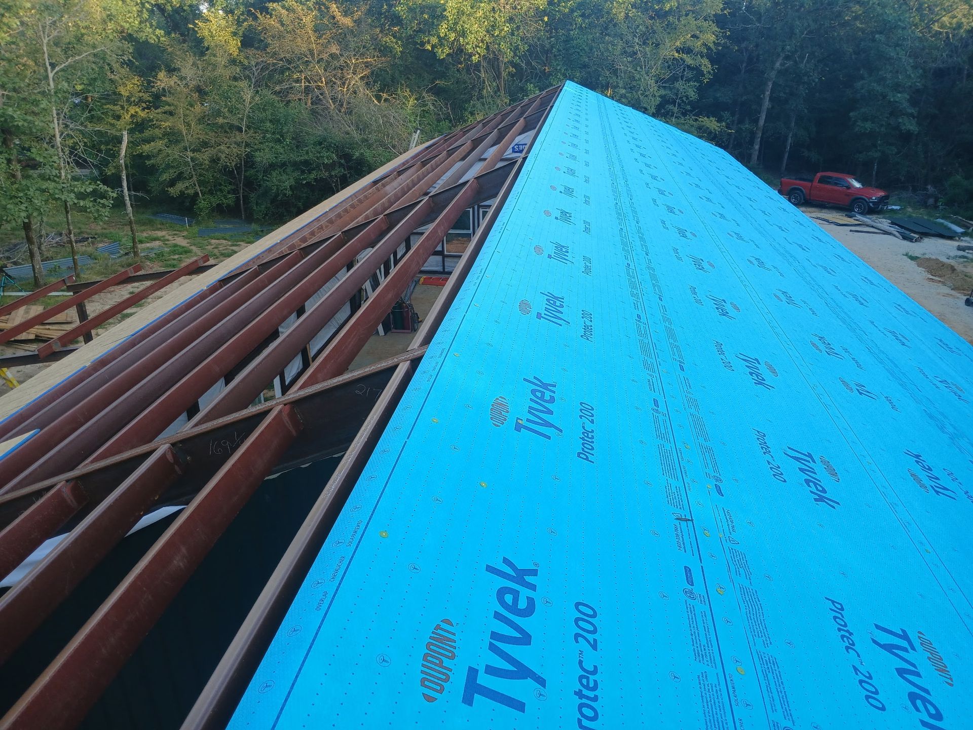 Blue Tyvek house wrap installed on a roof under construction, with exposed wooden framing.