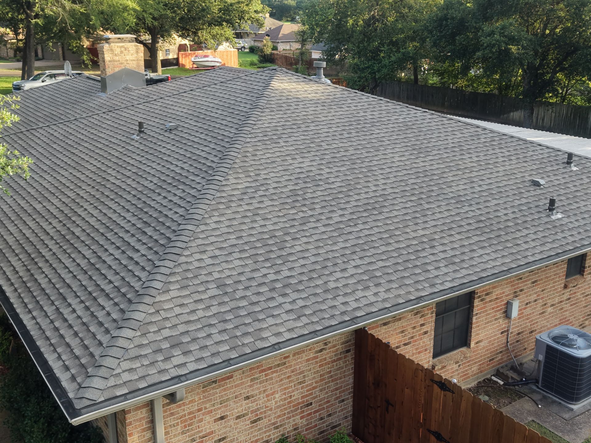 Aerial view of a house with a gray shingle roof, brick walls, and a fenced backyard.