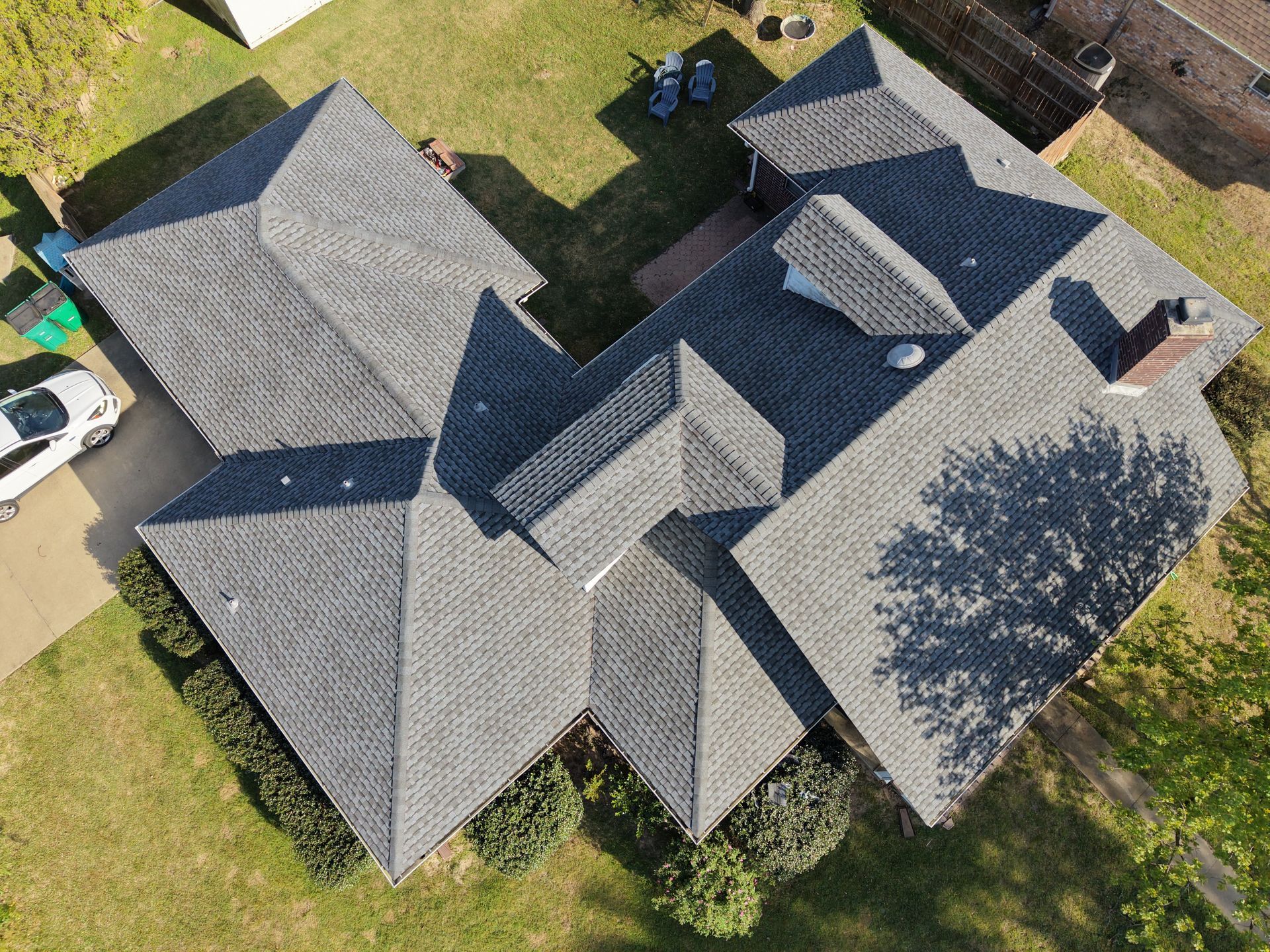 Aerial view of a gray-roofed suburban house with a driveway, lawn, and neighboring homes.