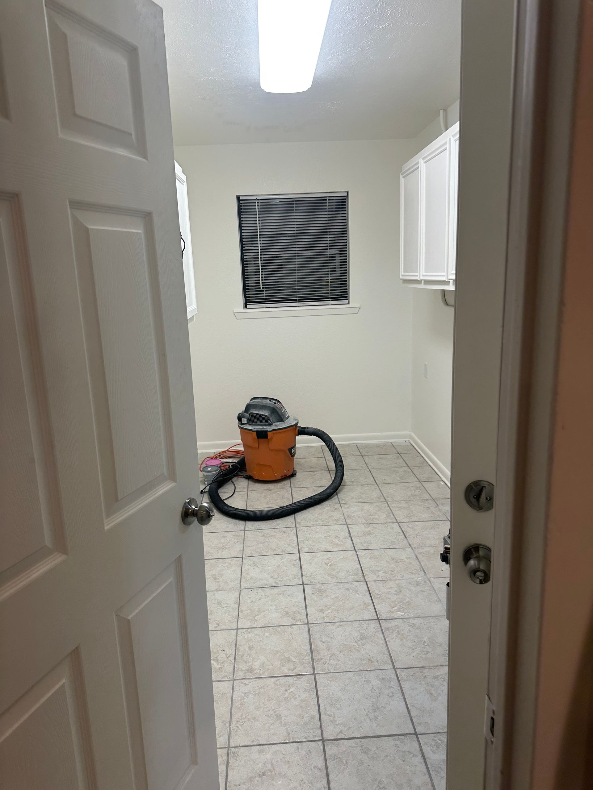 Small laundry room with a vacuum cleaner on tiled floor and a window covered by striped material