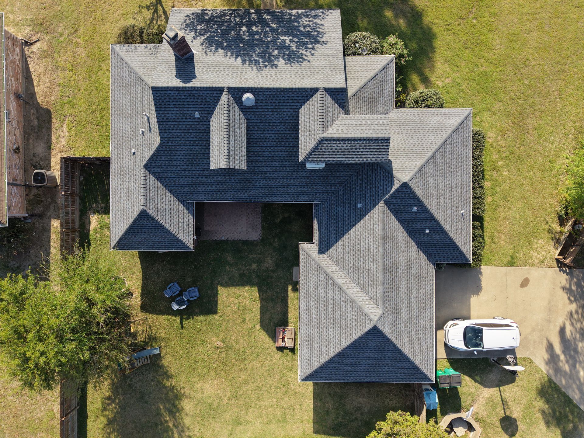 Aerial view of a gray-roofed house with lawn, driveway, and a white car parked outside