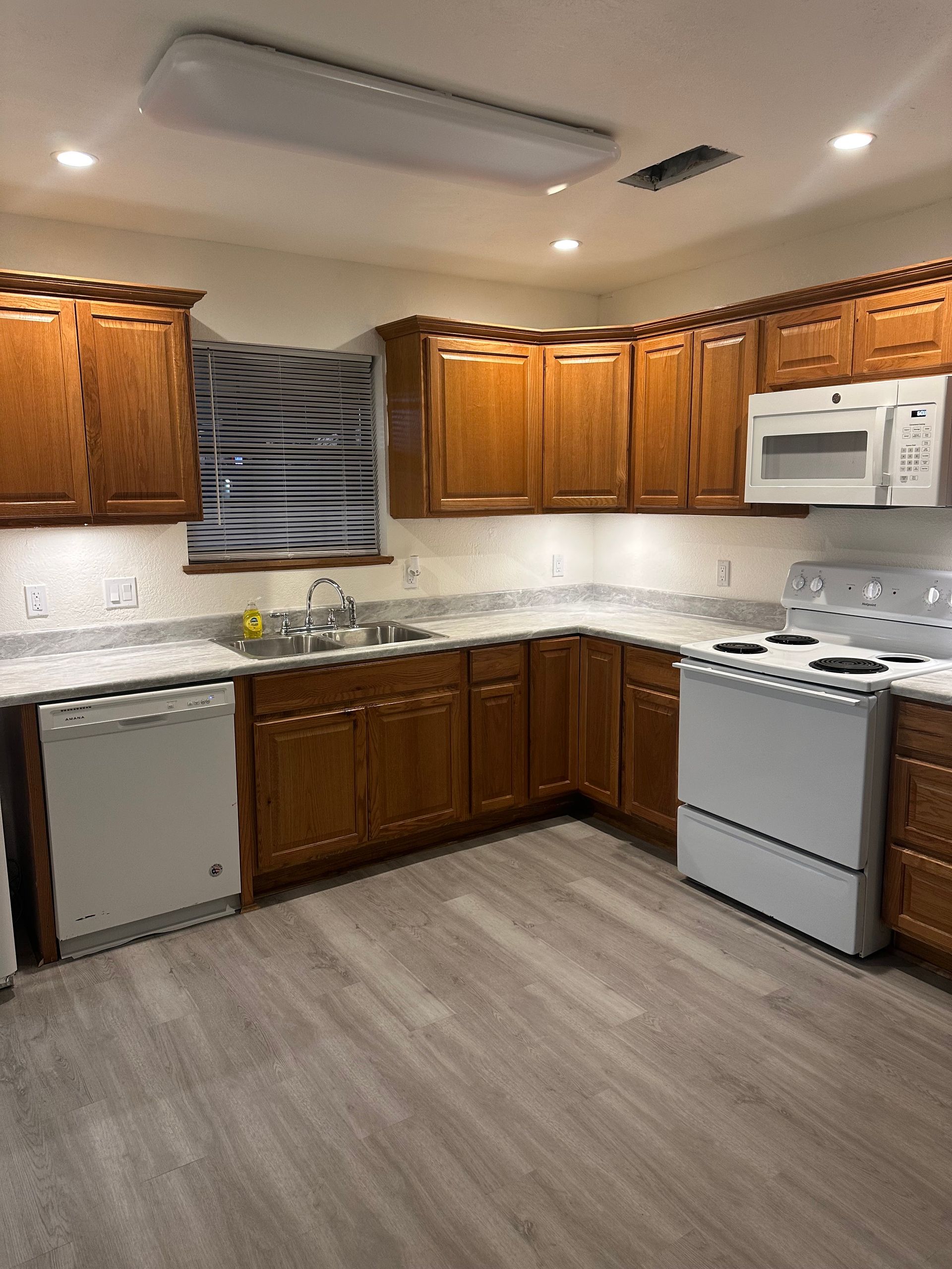 Kitchen with wood cabinets, white appliances, and gray flooring under bright overhead lights