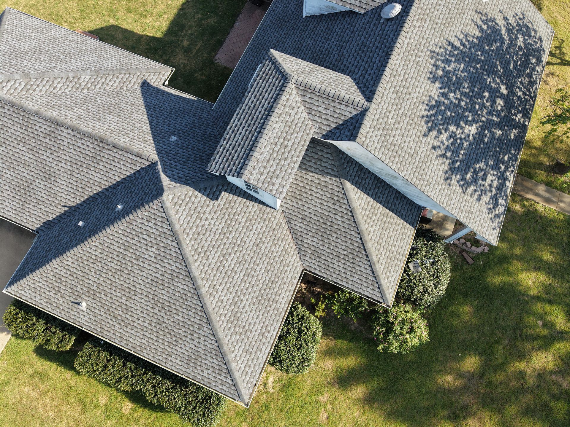 Aerial view of a house with a gray shingled roof and surrounding green lawn