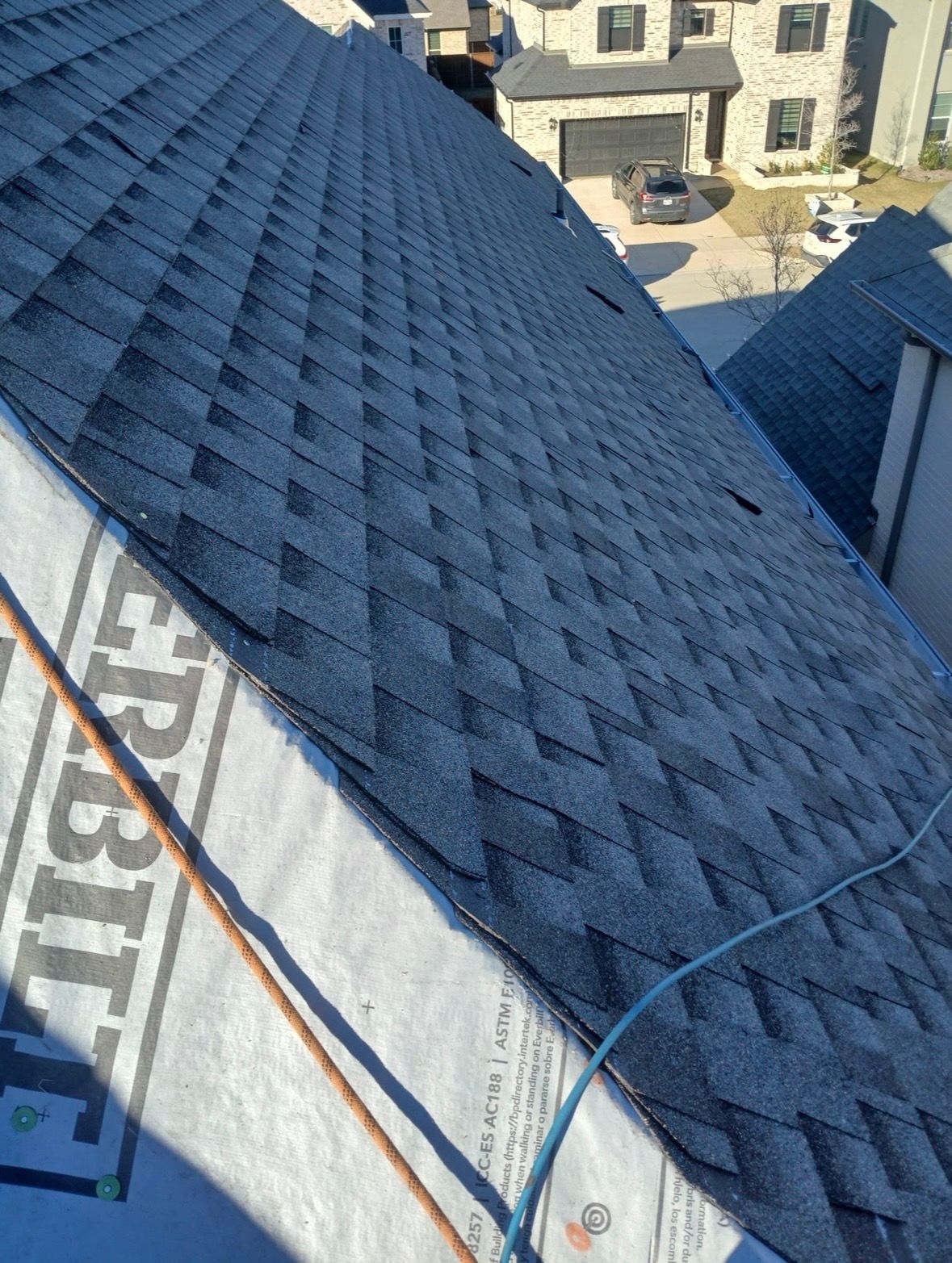 Blue shingled roof with underlayment and blue straps, viewed from above during construction