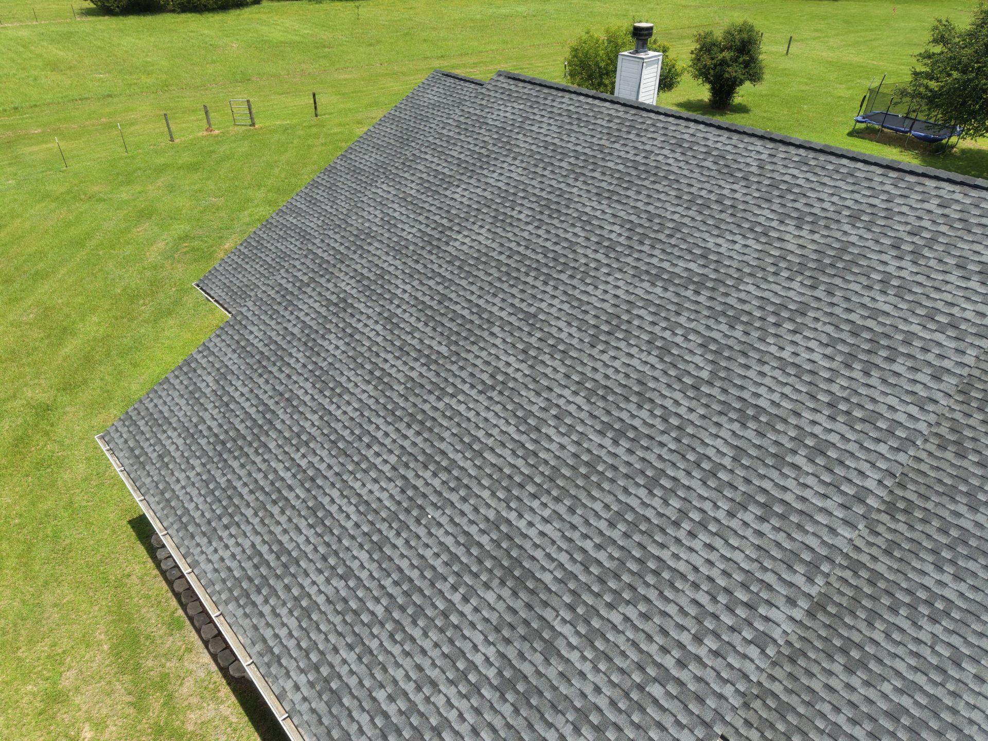 Aerial view of a gray shingled roof on a house beside a grassy yard and trees