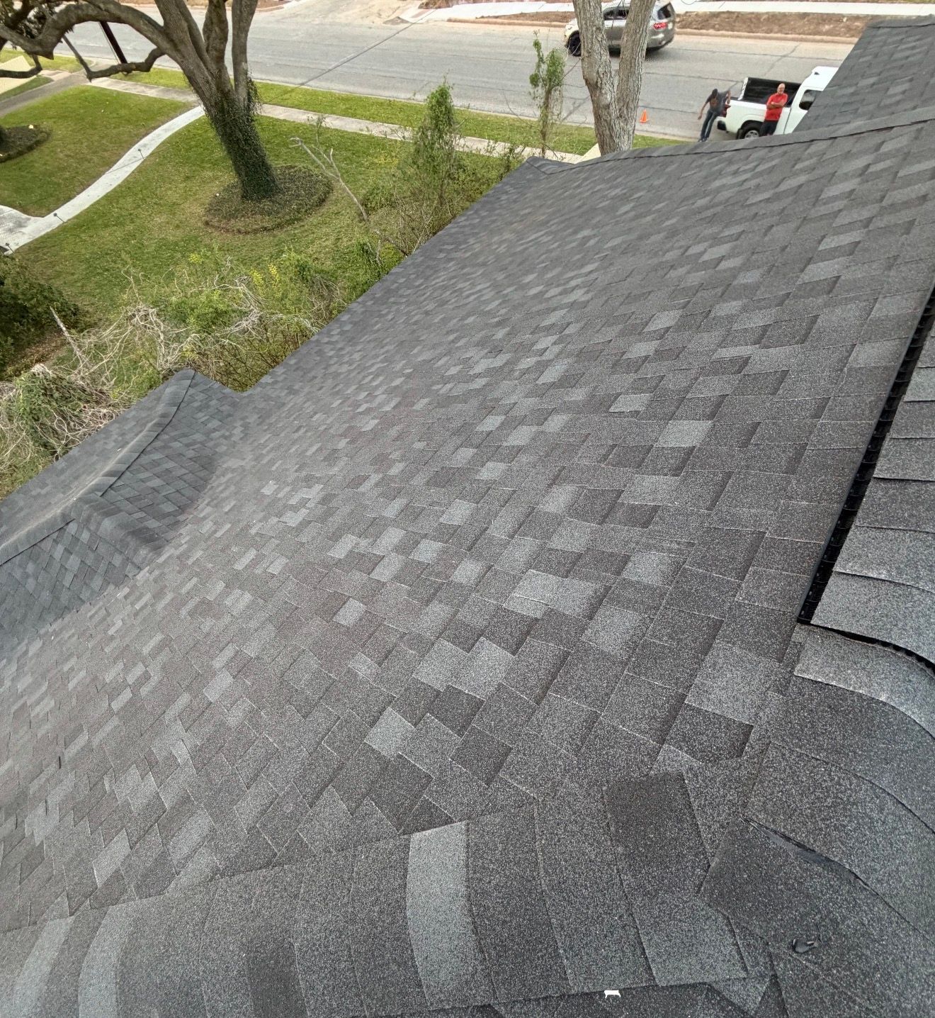 Close-up of gray asphalt shingle roof with a gutter, overlooking a yard and street below