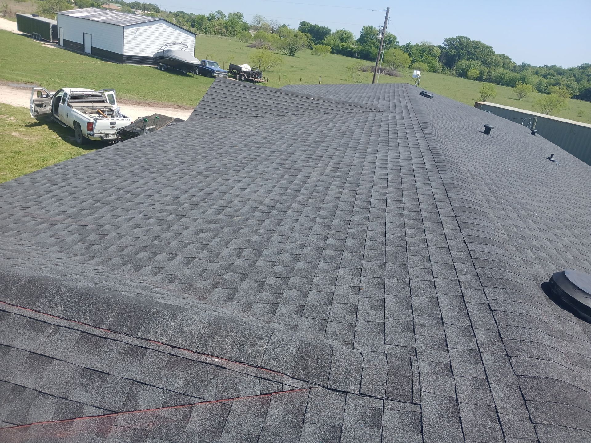 Roofing shingles on a house under construction, with a work truck and grassy yard in the background