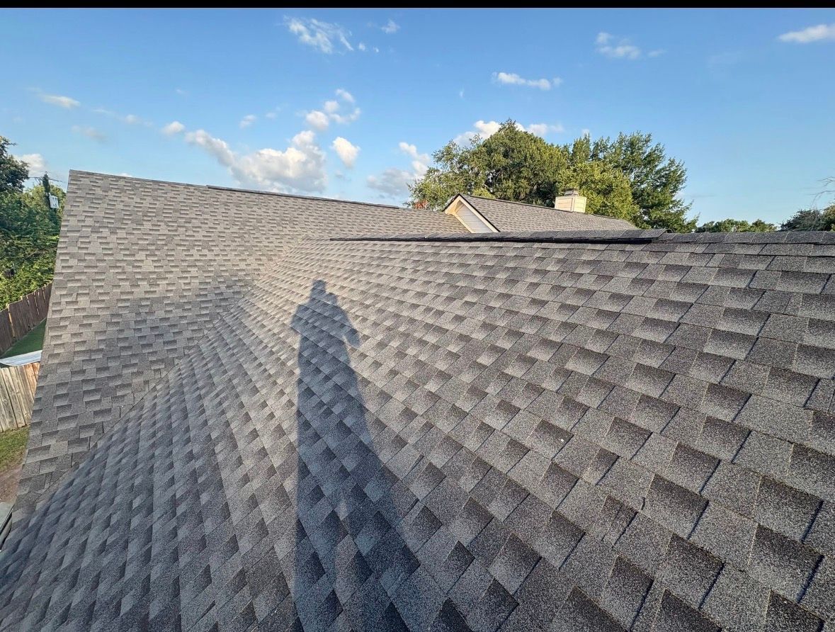 Gray shingled roof with a shadow, blue sky, and trees in the background
