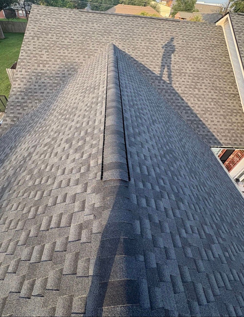 Roof shingles on a house, viewed from the ridge with a shadow falling across the slope.