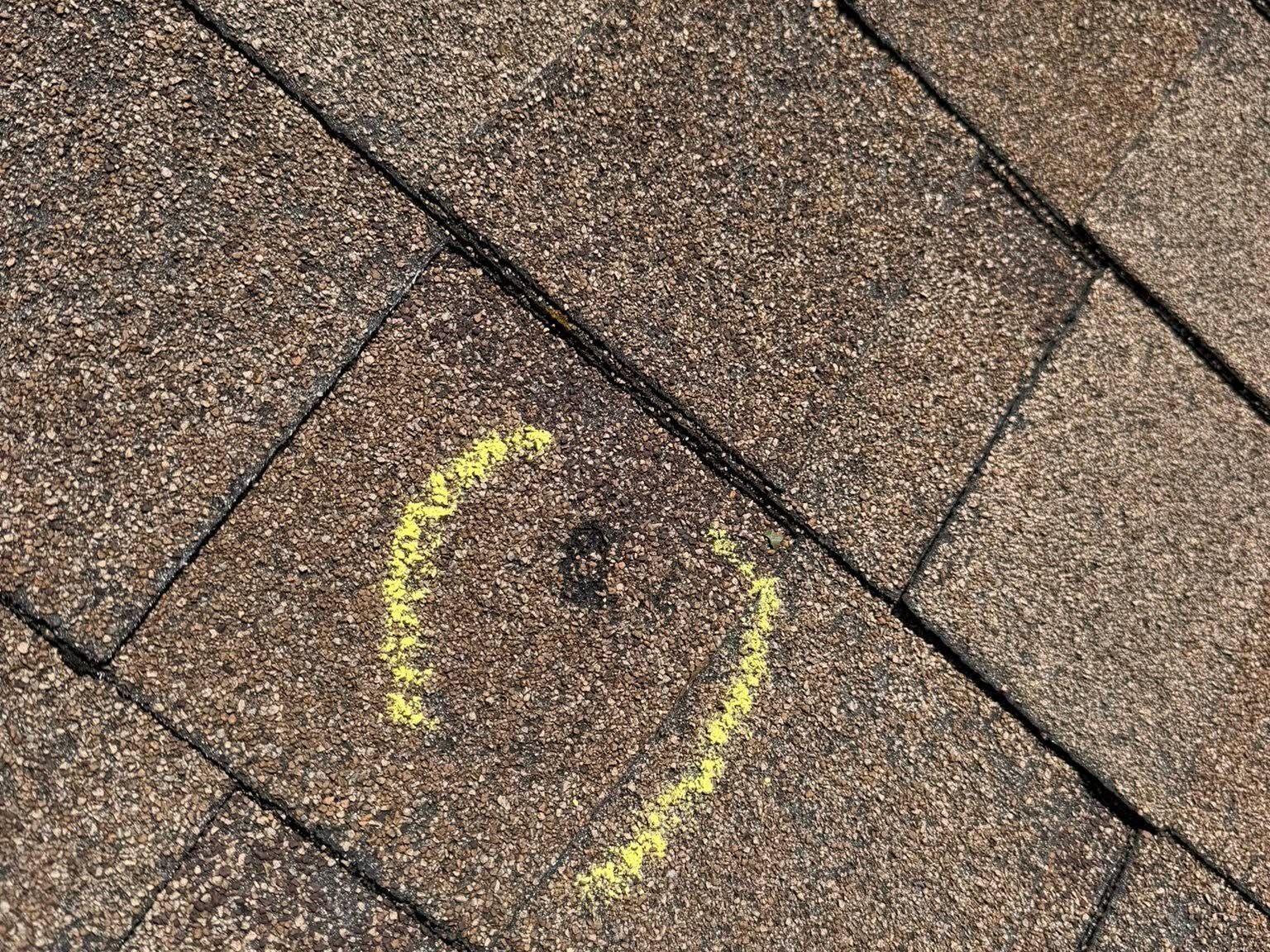 Close-up of brown roof shingles marked with a yellow chalk circle.