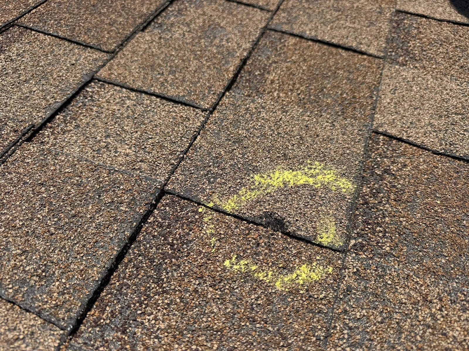 Close-up of brown roof shingles with yellow spray paint markings.