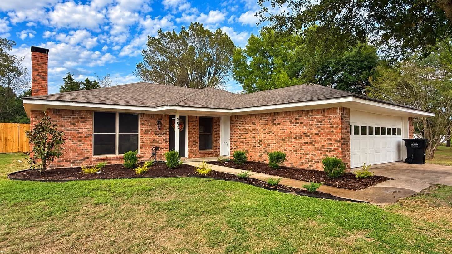 Brick ranch-style house with white garage, front lawn, and blue sky with trees