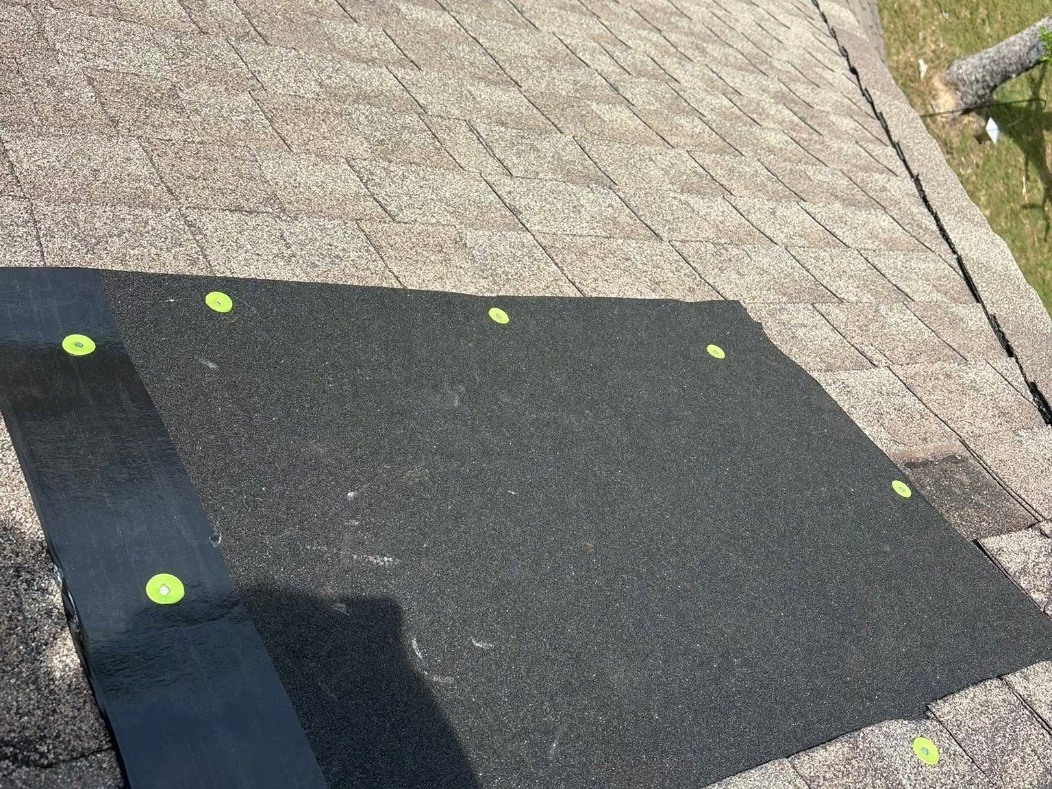 Black roof patch with lime-green fasteners on a shingled roof edge