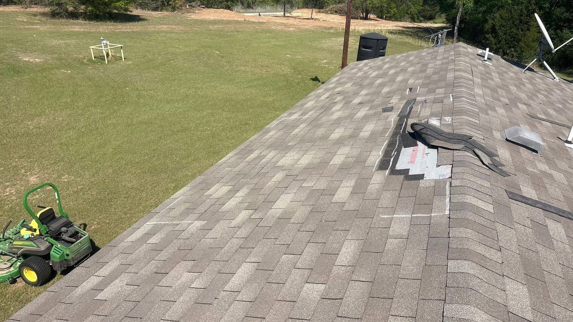 Roof shingles on a house with a lawn, a green mower in the yard, and a small white dog in the distance