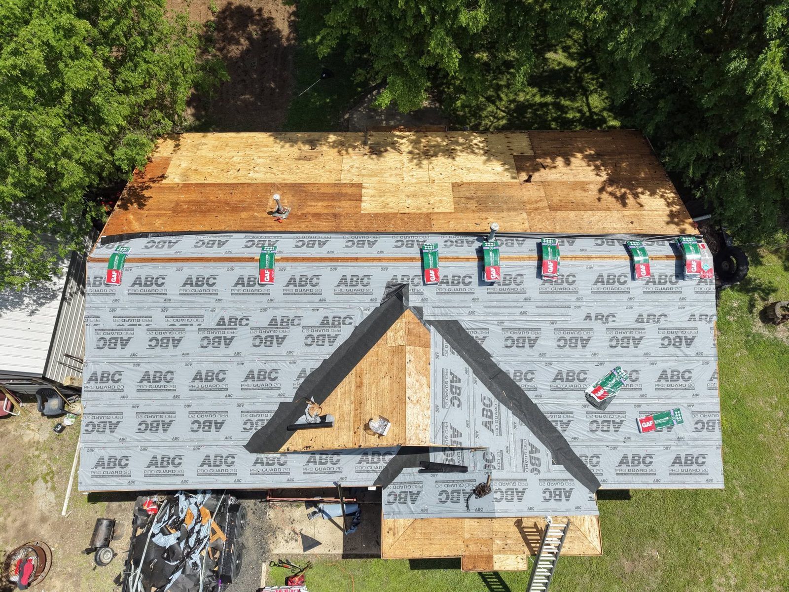 Roof under construction with gray underlayment, triangular dormer opening, and trees in the background