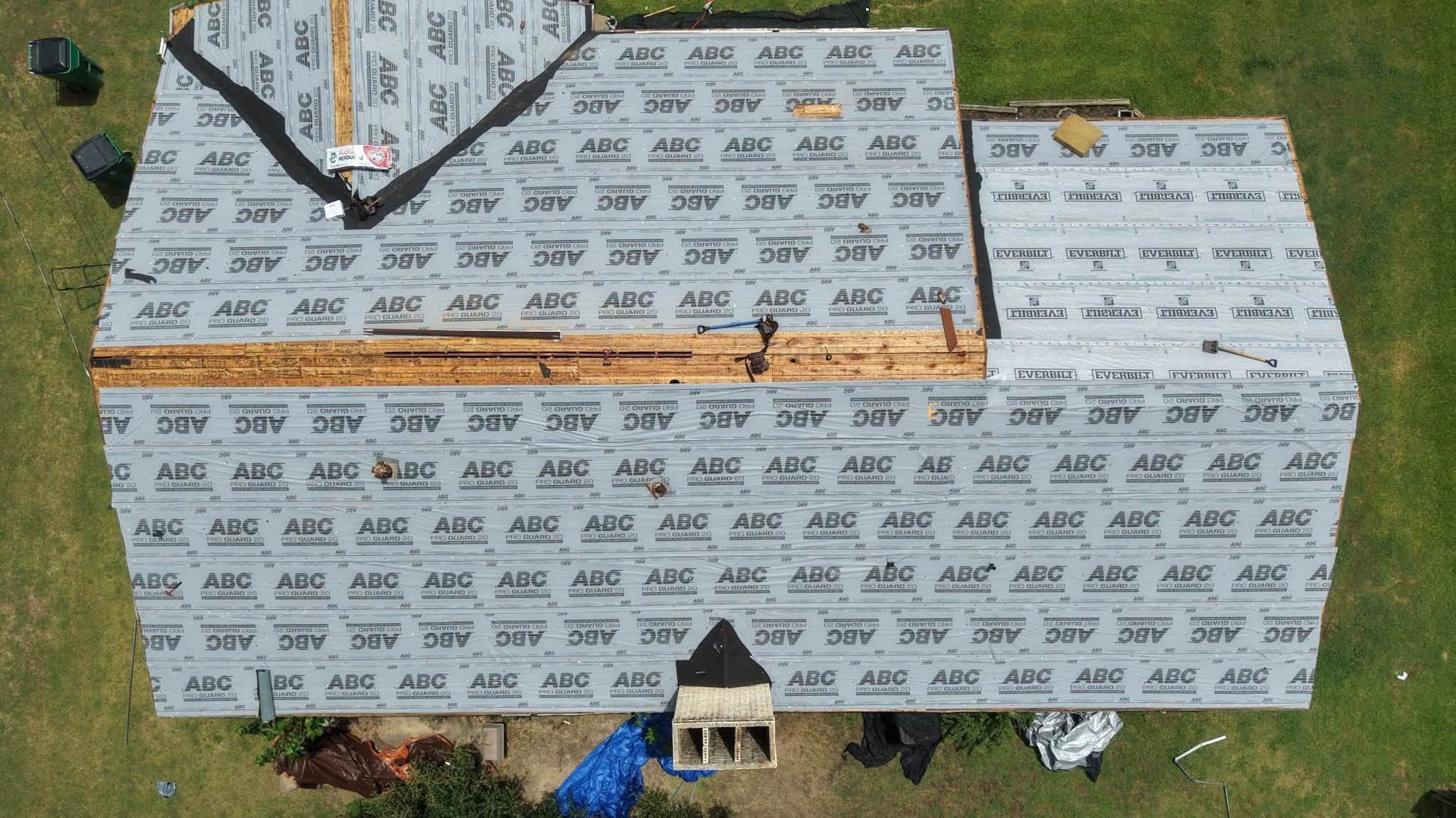 Partially covered house with gray siding wrap and roof under construction, viewed from above
