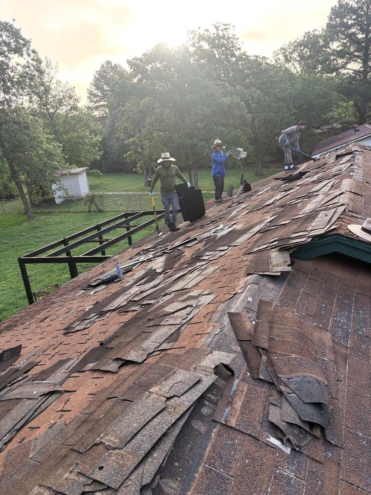 People inspecting a heavily damaged roof with missing shingles in a wooded area