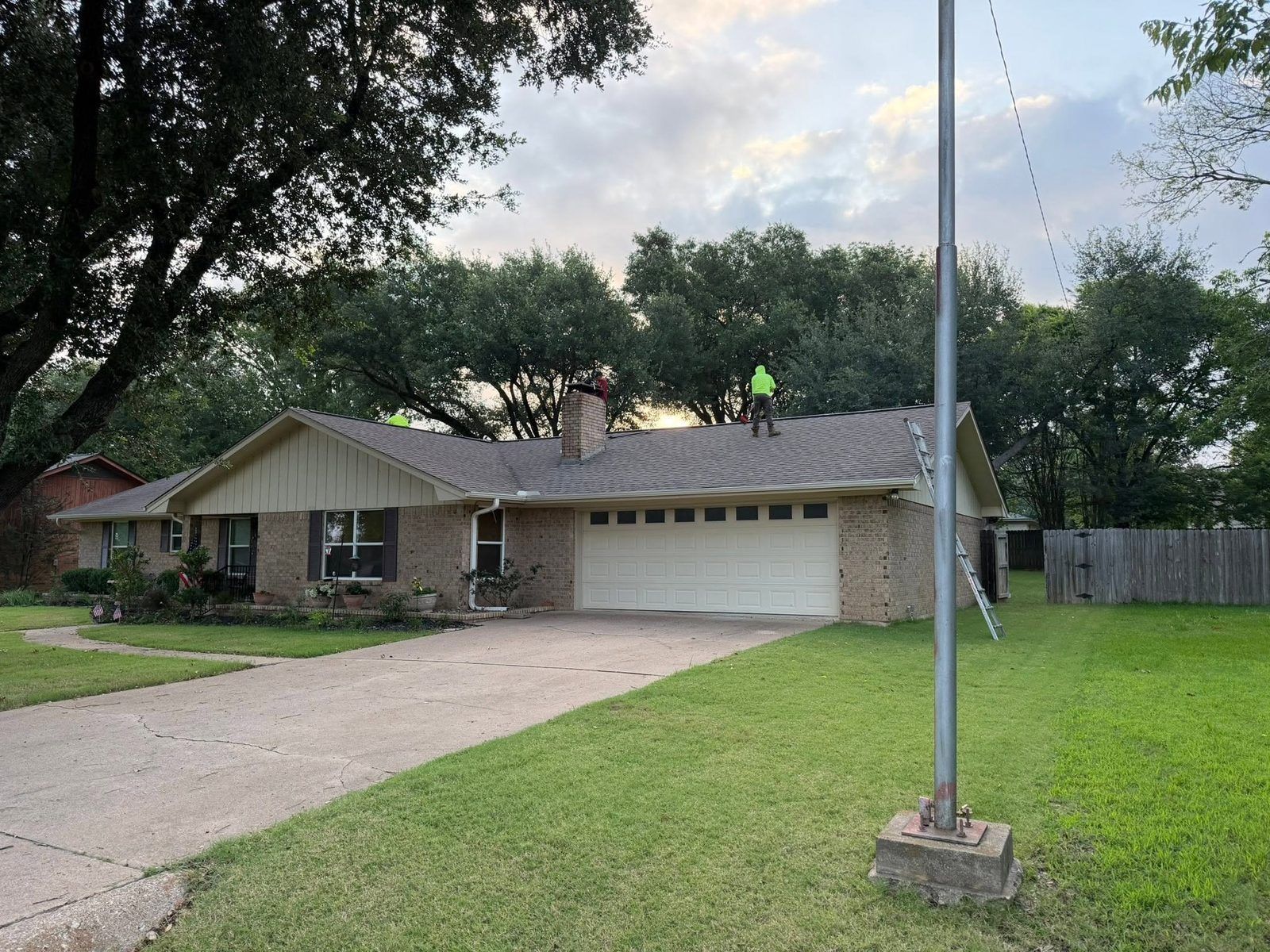 Single-story suburban house with a driveway, front lawn, and a flagpole at dusk