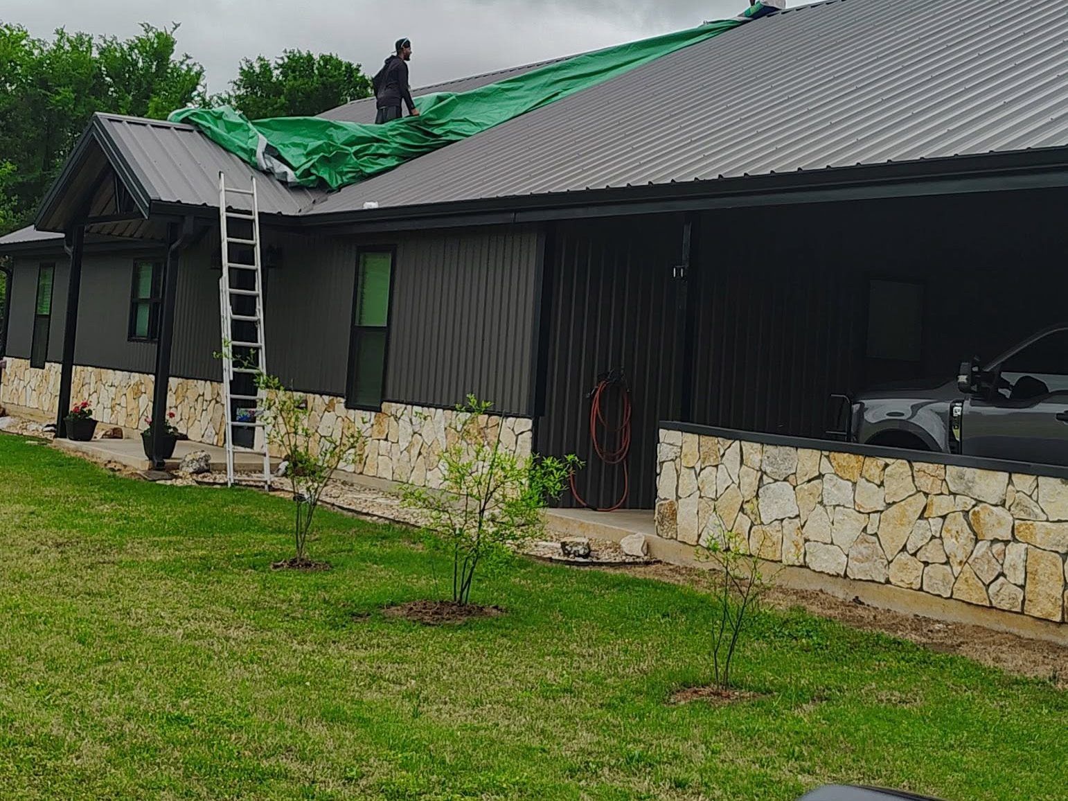 Storm-damaged house with a green tarp on the roof and a ladder leaning against the side