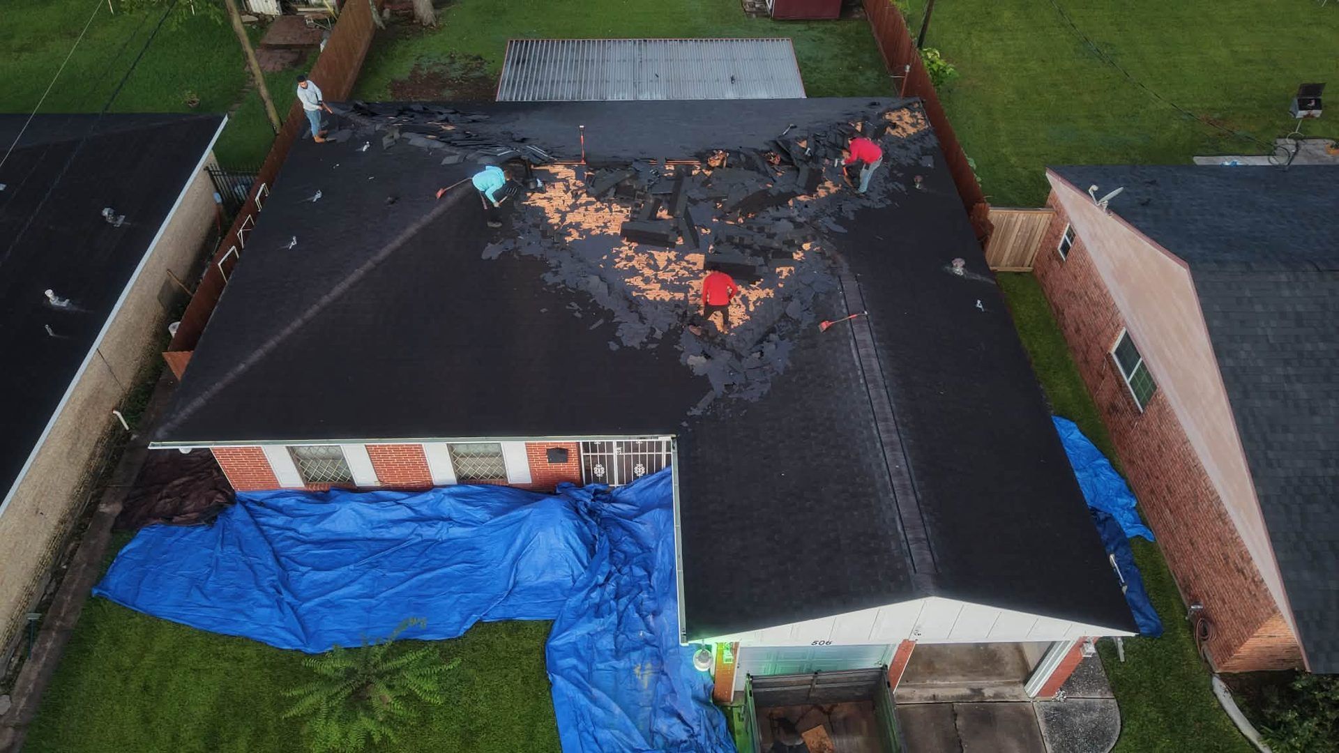 Aerial view of a house roof with storm damage and blue tarp covering the lower left section.