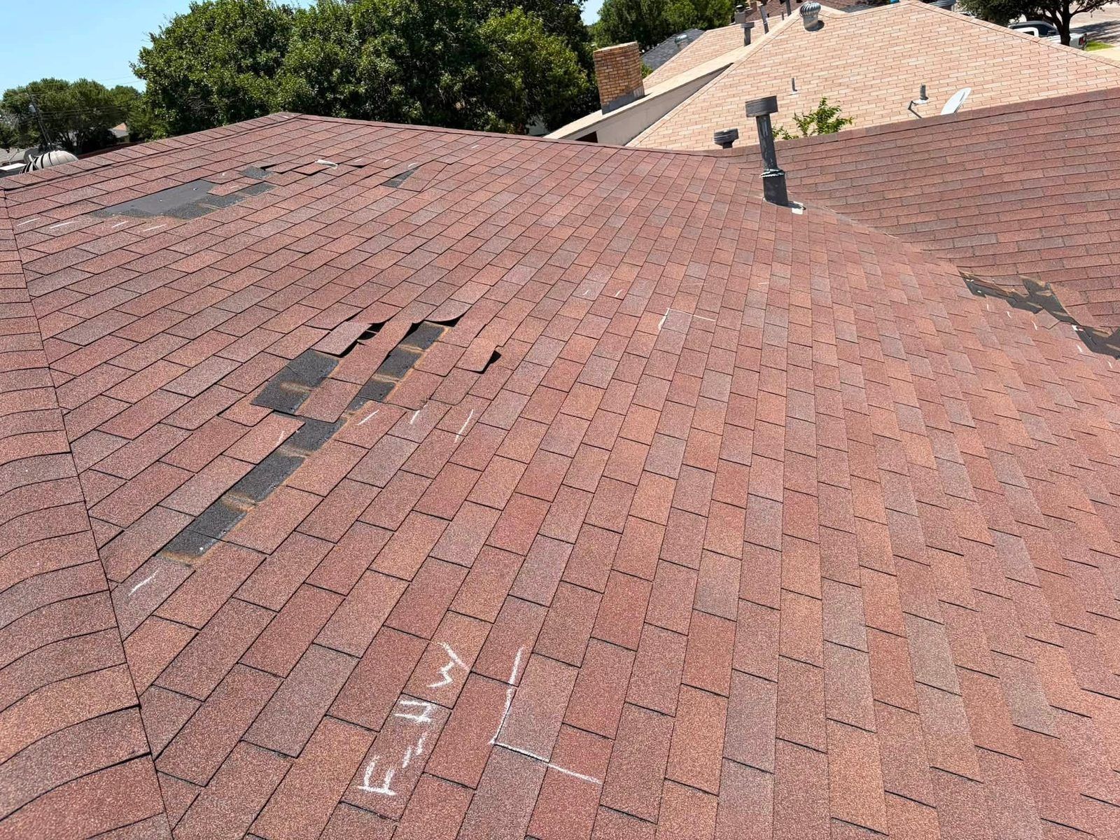 Red shingle roof with several missing or damaged sections under a clear sky.