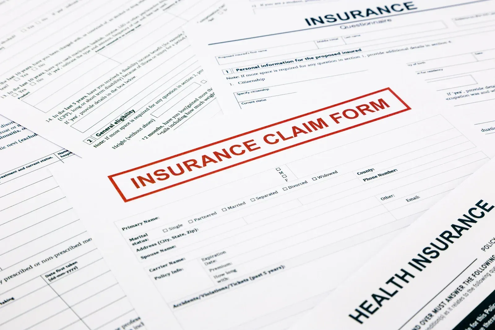 Insurance claim forms stacked on a desk, with one form stamped “INSURANCE CLAIM FORM” in red.