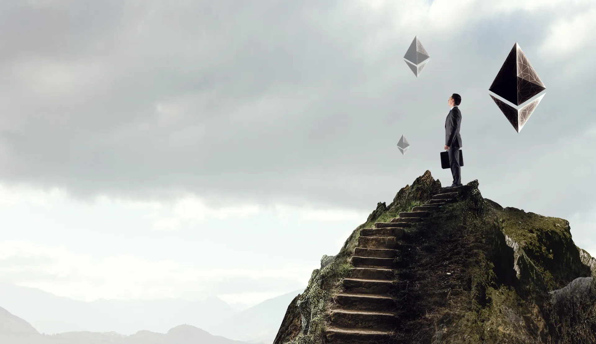A man is standing on top of a mountain with kites flying around him.