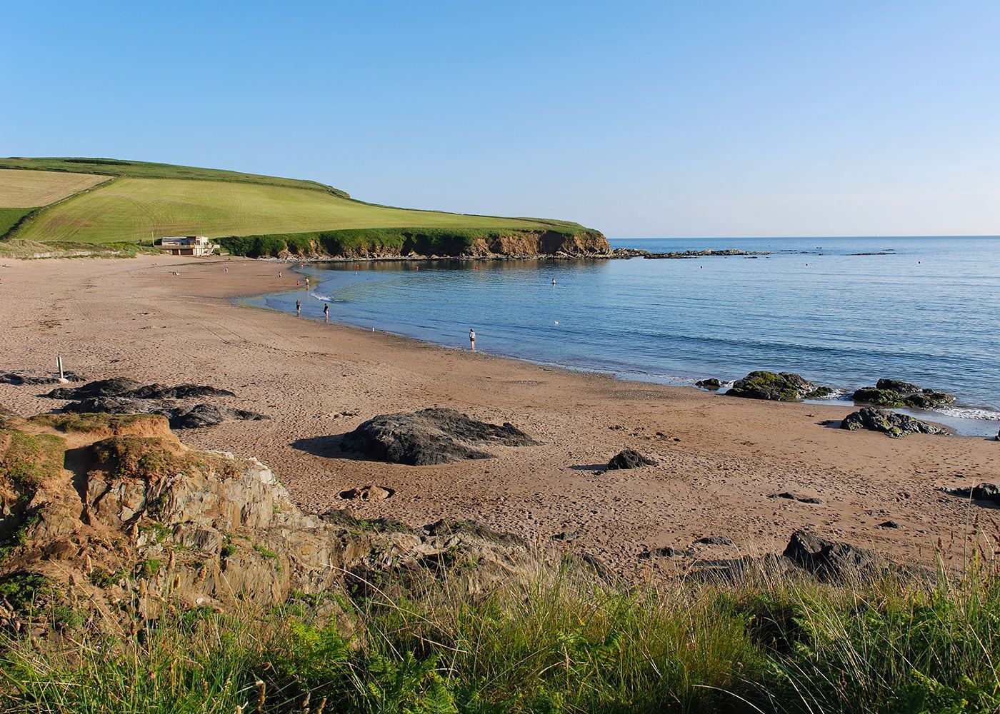 A sandy beach next to a body of water with a grassy hill in the background.