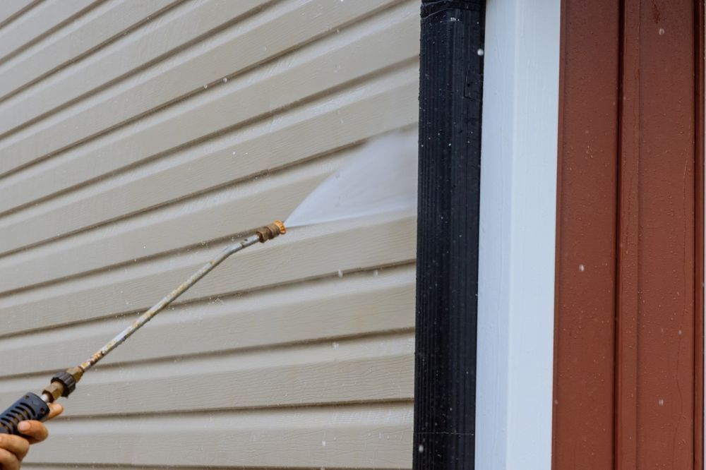 A person is using a high pressure washer to clean the side of a house.
