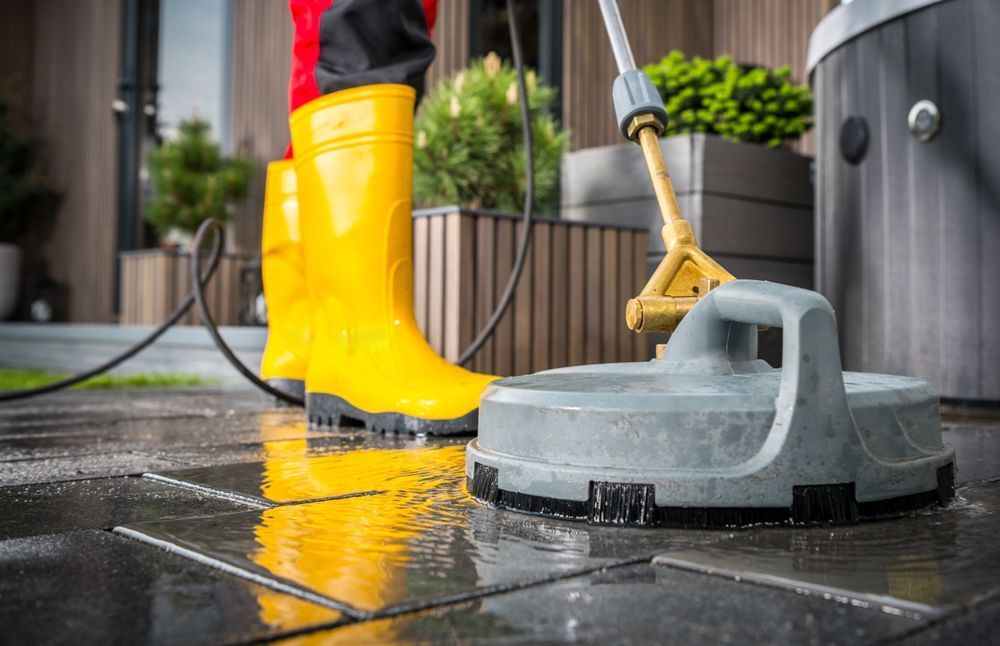 A person wearing yellow boots is cleaning a tiled floor with a high pressure washer.
