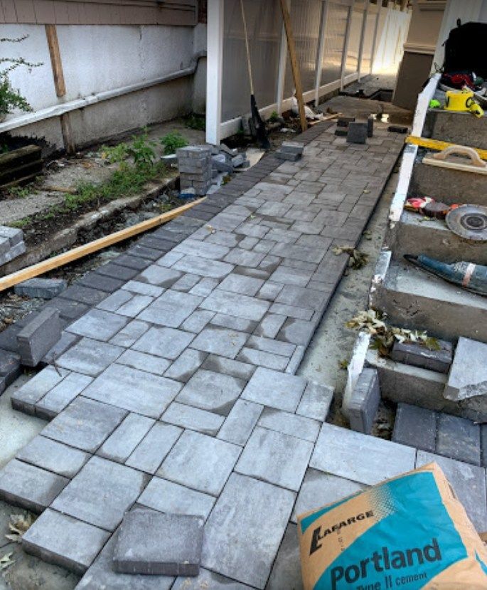 A bag of portland cement is sitting on the ground next to a brick walkway being built.