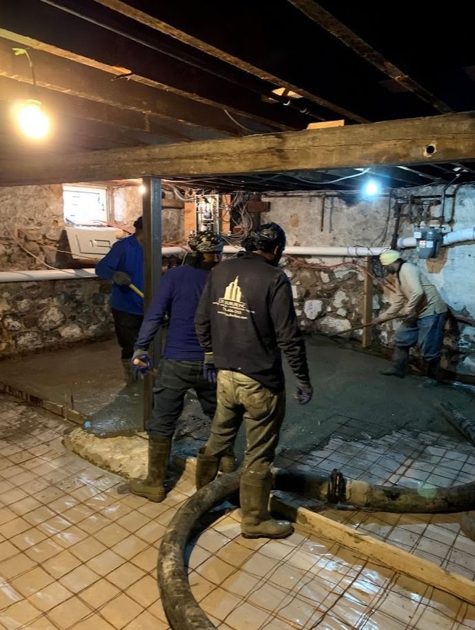 A group of men are working on a concrete floor in a basement at night.
