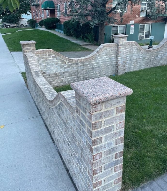 A brick wall surrounds a lush green lawn in front of a building.