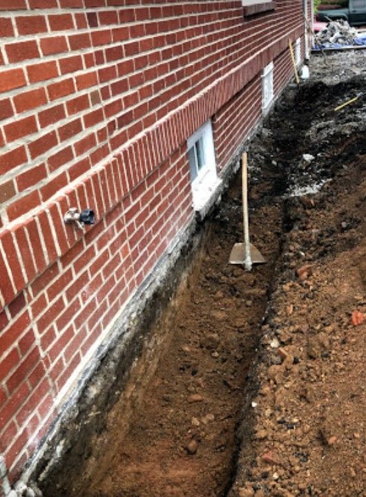 A shovel is sitting in the dirt next to a brick wall.