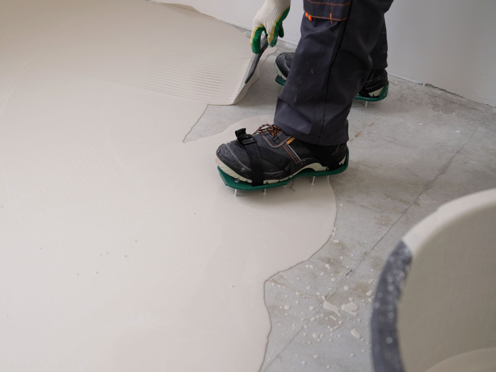 A person is applying a coating to a concrete floor with a spatula.
