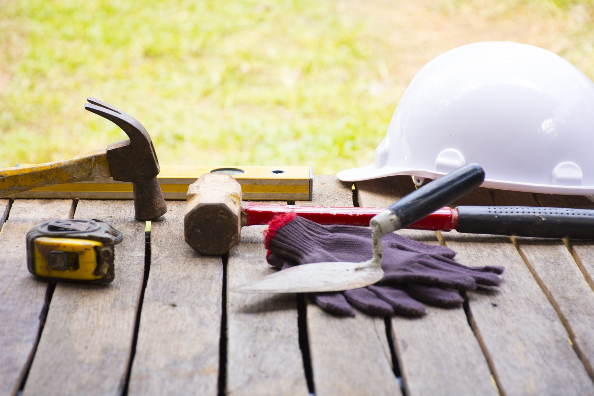 A hard hat , hammer , tape measure , gloves and other construction tools are on a wooden table.