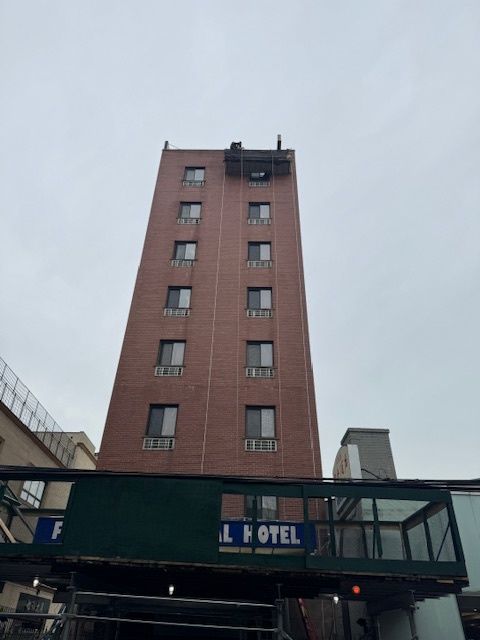 Tall brick hotel building with a green awning and a visible hotel sign, seen from below.