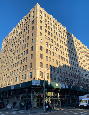 Tall beige corner building with scaffolding at street level under a blue sky