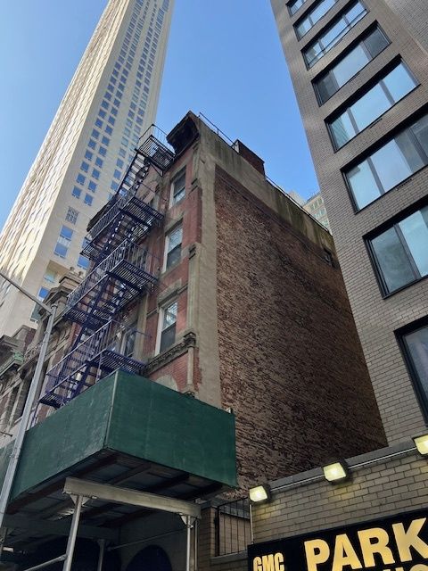 Tall city buildings with a brick wall, fire escape, and a green construction awning below.