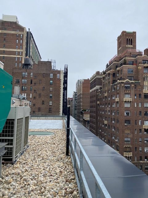 Rooftop view of brick apartment buildings under a cloudy sky, with HVAC units and gravel foreground