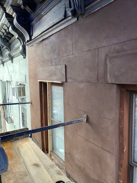 Exterior building wall with windows and a long metal beam extending from a scaffold walkway.