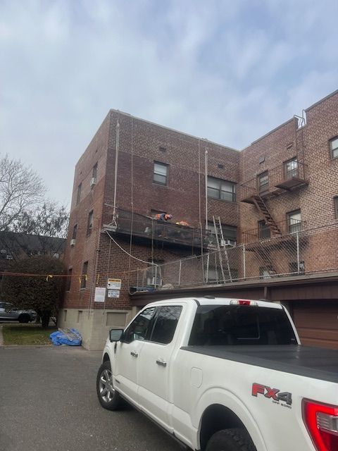 White pickup truck parked beside a brick apartment building under a cloudy sky.