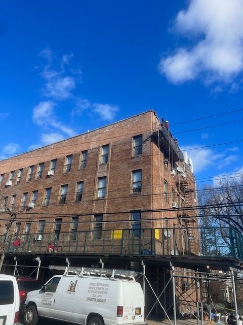 Brick apartment building under renovation with scaffolding and parked vans on a city street