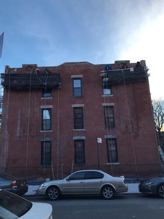 A white car is parked in front of a large brick building.