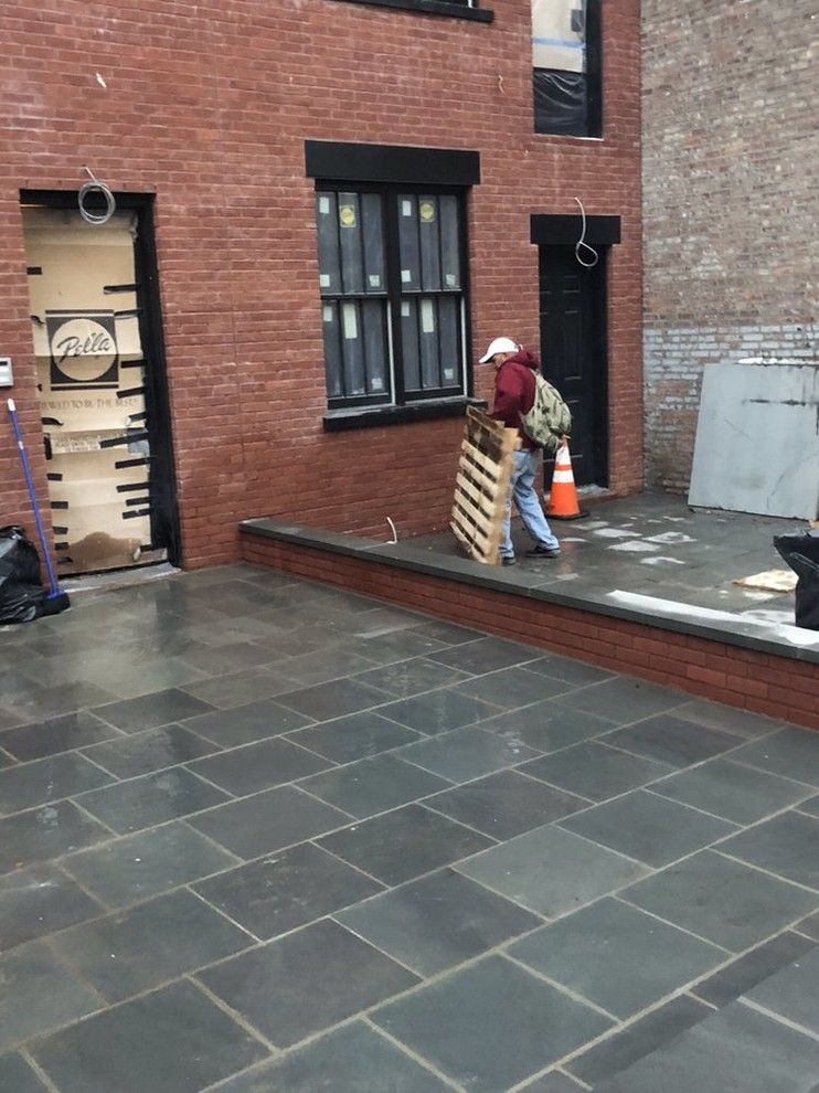 A man is carrying a wooden pallet in front of a brick building